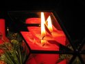 Das Bild einer auf einem Adventskranz sitzenden Kerze wird in einem Bleiglas vervielfacht