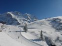 Skihang mit abfahrenden Skifahrern mit einem Berg im Hintergrund und einem Hügel auf der rechten Seite.