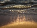 Blick auf von den Wellen benässten Sandstrand bei Sonnenaufgang. Hier lässt die Sonne den Sand golden erscheinen.