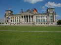 Der Reichstag mit wehenden Flaggen bei strahlend blauem Himmel und vereinzelten Schönwetterwolken