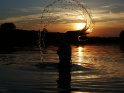 Frau schleudert bei Sonnenuntergang im Wasser ihre Haare so zurck, dass sich ein Kreis aus Wasser um ihren Kopf bildet.