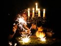 Eine Frau im Hexenkostüm mit Kerzenleuchter, Glaskugel, Kürbissen und Wunderkerzen
