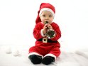 Niedliches Baby im Weihnachtskostüm spielt mit einer Glocke.