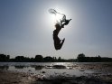 Frau in Bikini springt an einem See mit einem blauen Seidentuch in die Luft.