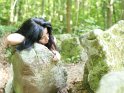 Schwarzharige Frau liegt auf einem Felsen im Wald