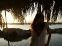 Eine Frau im weißen Strandkleid steht kurz vor Sonnenuntergang am Meer. Hinter ihr befindet sich das Meer.