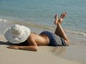 Junge Frau liegt mit Badehose und Sonnenhut am Strand