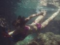 Junge Frau im lila Bikini taucht mit einem bunten Tuch im Meer