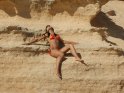 Braungebrannte Frau im rot-gelben Bikini sonnt sich in einer Sandsteinwand.