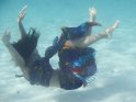 Unterwasserfoto einer in bunte Tücher gehüllten Frau, die sich im Wasser fallen lässt.