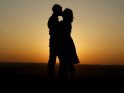 Foto von einem Pärchen, das sich vor einem Sonnenuntergang küsst. Von den beiden Liebenden sind lediglich die Umrisse zu erkennen.