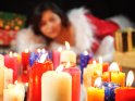 Junge Frau im Weihnachtskostm liegt hinter einem groen Haufen brennender Kerzen. Drum herum sind diverse Weihnachtsgeschenke aufgestapelt.