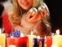 Frau im Weihnachtskostüm mit brennenden Kerzen und Weihnachtskugeln
