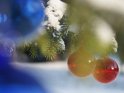 Weihnachtsbild mit farbigen Glaskugeln an einem mit Schnee bedeckten Tannenzweig