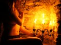 Teilaktfoto einer Frau, die im Licht eines Kerzenleuchters in einer Mauernische sitzt.