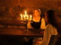 Zwei Frauen in mittelalterlicher Gewandung sitzen im Licht eines Kerzenleuchters an einem Holztisch auf einer Burg.
