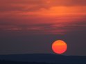 Der rote Ball der Sonne bewegt sich bei Sonnenuntergang auf einen Hügel zu.