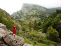 Frau im roten Kleid läuft auf Felsen vor einer imposanten Berglandschaft herum.