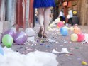 Frau läuft durch eine Straße mit herumfliegenden Luftballons und Konfetti.