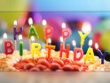Geburtstagskarte mit brennenden Kerzen auf einer Torte. 
Die Kerzen bilden den Schriftzug Happy Birthday