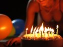 Erotisches Foto einer Frau in Dessous, die hinter einer Torte mit brennenden Geburtstagskerzen kniet.