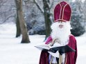 Der Nikolaus steht in einer winterlichen Landschaft und liest aus einem dicken Buch.