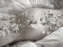 Foto einer Frau, die nur von zahlreichen Federn bedeckt auf dem Bauch im Bett liegt.