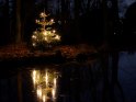 Ein Weihnachtsbaum spiegelt sich bei Nacht mit seinen brennenden Kerzen im Wasser.