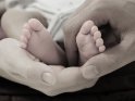 Die Füße eines 24 Tage alten Säuglings liegen in den Händen seiner Eltern