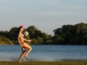 Frau im Fußball-Bikini spielt Fußball an einem See.