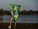 Eine Frau steht am See auf einem Fußball und hält eine Brasilien-Flagge in die Luft.