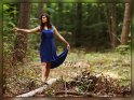 Tnzerin balanciert im blauen Abendkleid auf einem Baumstamm im Wald.
