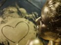 Eine Frau mit Goldbodypainting hat ein goldenes Herz auf den Boden gemalt.