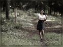 Frau in Rock und Bluse steht im Wald auf einem Waldweg und spielt mit ihren Haaren.