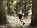 Junge Frau springt im Wald zwischen zwei Bäumen freudestrahlend in die Luft.