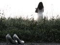 Eine junge Frau steht nach dem Ausziehen ihrer Highheels auf einer Wiese. Die Schuhe sind im Vordergrund des Bildes zu sehen.