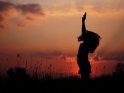 Frau springt vorm Sonnenuntergang auf einer Wiese in die Luft