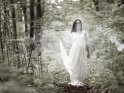 Eine Frau steht in einem Hochzeitskleid, gehllt in Nebel, im Wald.