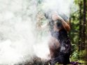 Eine Hexe im Wald macht beschwörerische Handbewegungen, umgeben von Rauch- oder Nebelschwaden,