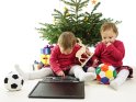 Zwillinge sitzen unterm Weihnachtsbaum mit ihren Geschenken und zerstören dabei ein Notebook.