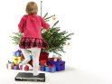 Lustiges Foto von einem kleinen Mädchen, das vor einem Weihnachtsbaum unter dem viele Geschenke liegen, auf einem Notebook herumhüpft.