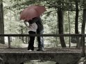 Schwangeres Paar küsst sich unter einem Regenschirm auf einer Brücke