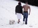 Foto von einem Pärchen, dass mit einem Hund durch den Schnee läuft. Der Mann hat der Frau, die nur ein Kleidchen trug, seine Jacke gegeben und stapft nun mit freiem Oberkörper durch den Schnee.