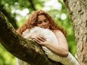 Eine junge Frau hat es sich mit einem weißen Kissen auf einen Baum bequem gemacht.
