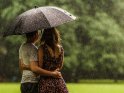 Paar steht aneinander gekuschelt unter einem Regenschirm in strömendem Regen
