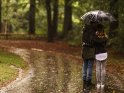 Paar steht aneinandergekuschelt im Regen unter einem Regenschirm.