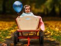 Ein Kleinkind sitzt mit einem Luftballon in einem Bollerwagen und streckt die Zunge heraus.