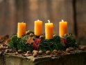 Im herbstlichen Wald auf einem steinernen Tisch stehender Adventskranz mit drei brennenden Kerzen zum 3. Advent.