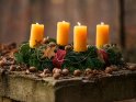 Im herbstlichen Wald auf einem steinernen Tisch stehender Adventskranz mit vier brennenden Kerzen zum 4. Advent.