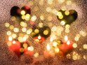 Herzen auf einer Fensterscheibe mit künstlichem Schnee. In der Glasscheibe spiegeln sich rote Kerzen und im Hintergrund sieht man die unscharfen Lichter eines Weihnachtsbaums.